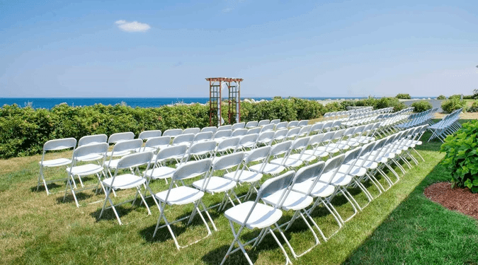 Ceremony setup at Bass Rocks with white folding chairs facing a wooden arch, overlooking the Atlantic Ocean